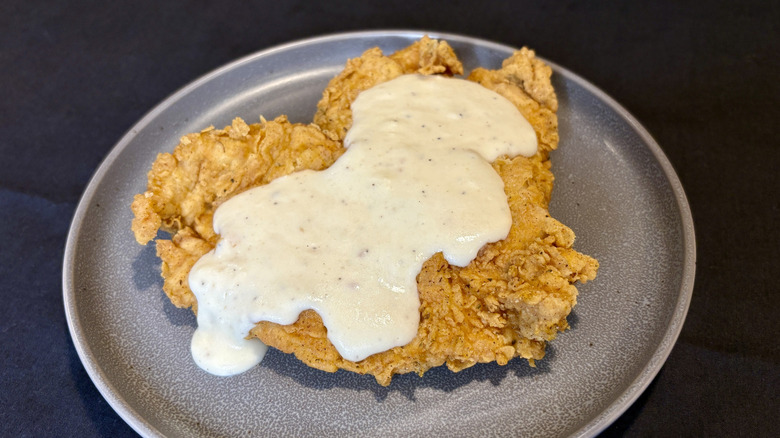 A piece of fried chicken with white gravy on a plate
