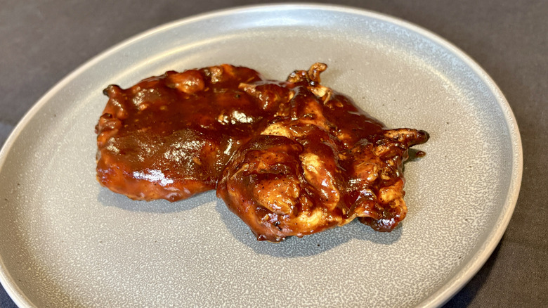A piece of chicken covered in barbecue sauce on a gray plate