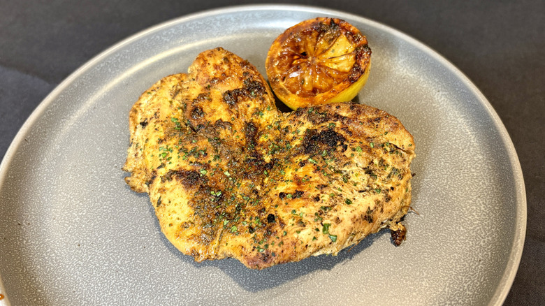 A seasoned chicken breast with half a grilled lemon on a gray plate