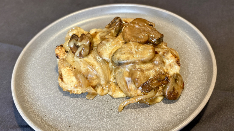 A piece of chicken covered in mushrooms, gravy, and cheese on a plate