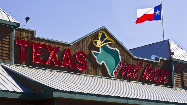 The exterior of a Texas Roadhouse restaurant with signage and Texas flag during daytime.