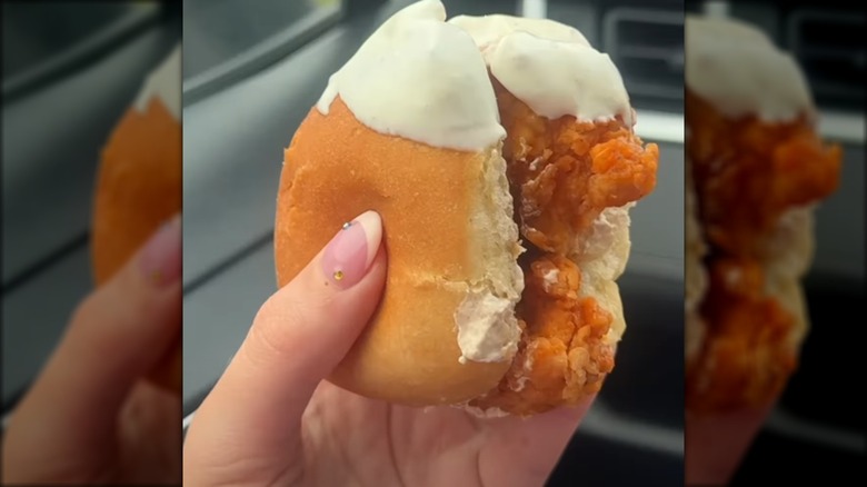 Hand holding a small Buffalo chicken sandwich with ranch dressing smeared on one end
