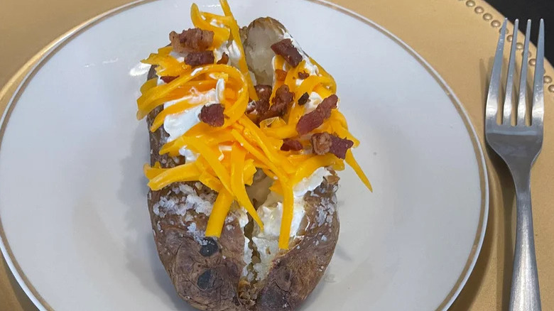 Texas Roadhouse loaded baked potato on a white plate with a fork on the side