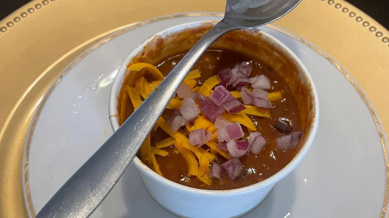 Texas Roadhouse chili in a white cup on a white plate with a spoon