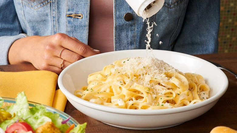 Olive Garden server grating Romano cheese over pasta for customer.