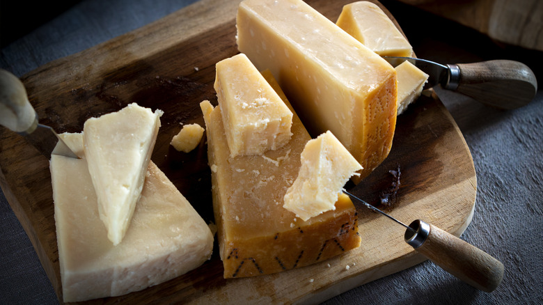 Hard Italian cheeses on wooden cutting board with knives.