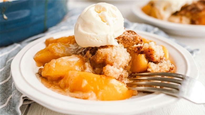 peach cobbler on white plate, scoop of vanilla ice cream on top