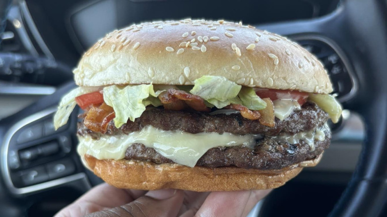 A hand holding a Peppercorn BLT Whopper in a car