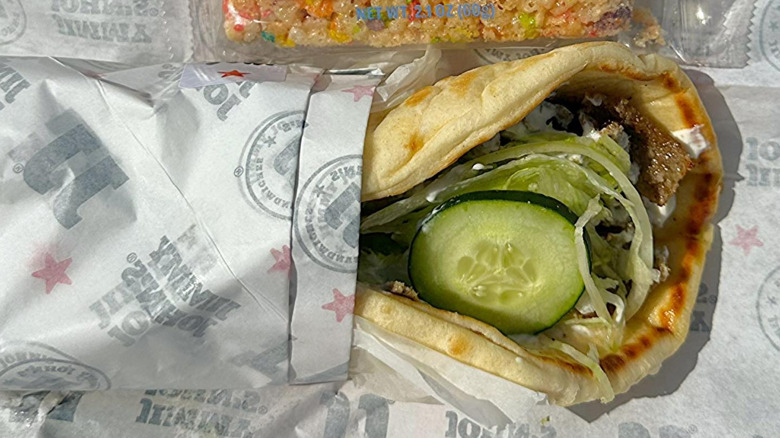 A gyro from Jimmy John topped with lettuce and cucumber in its branded paper wrapper