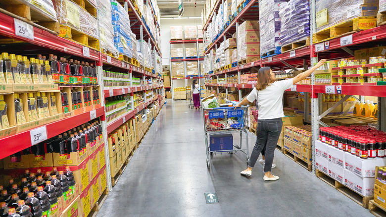 Sam's Club customer with one hand on their cart as they select a product from the shelf.