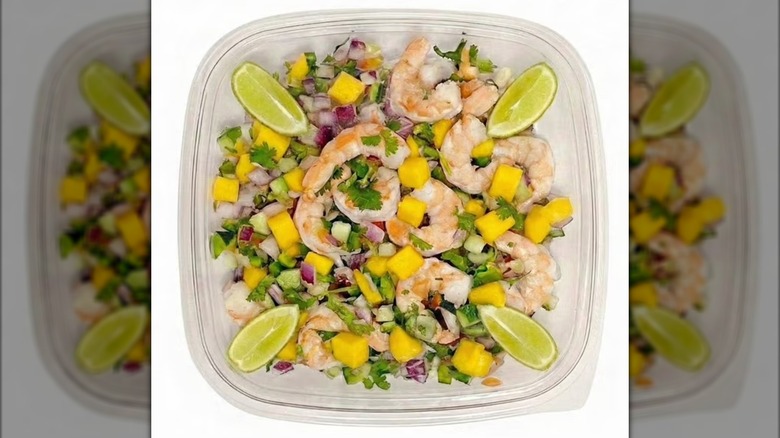 Plastic container with shrimp ceviche and lime wedges.