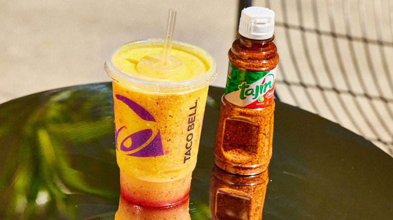 Taco Bell Tajín Pineapple Strawberry Freeze in takeout cup nex to bottle of Tajín seasoning