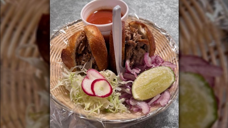 a traditional Guadalajaran torta ahogada in basket with side of sauce, lettuce, red onion, radish, and lime wedge