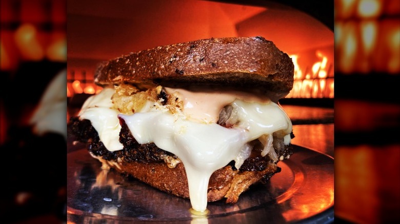 a thick Reuben sandwich with melted cheese on plate in front of burning fireplace in restaurant