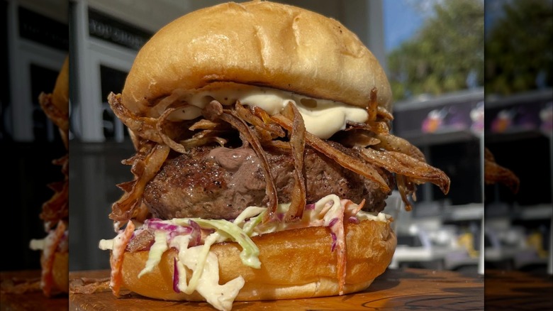 a close up of massive French onion hamburger on a toasted bun with coleslaw and sauce, set on wooden board outside