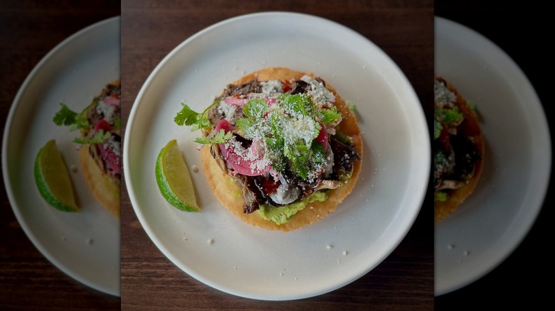 roasted mushrooms with red onion and avocado on tostada on white plate on wooden table