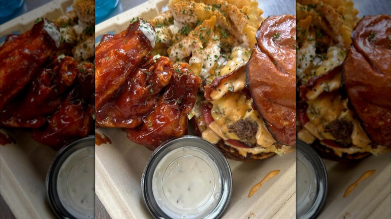 close up of saucy wings, French fries, and a cheesy chicken sandwich with bacon in takeout container with to-go container of ranch
