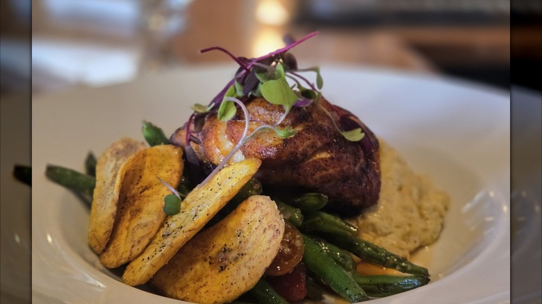 Blackened grouper, green beans, plantain mash, and sauce on white dish
