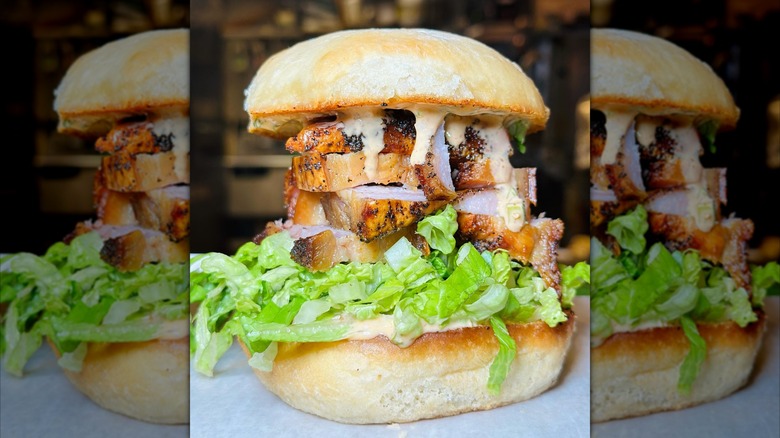 Crispy porkbelly with sauce and lettuce on bun in towering sandwich