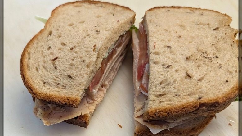 Smoked turkey sandwich with mayo and tomatoes on whole grain bread, on parchment paper