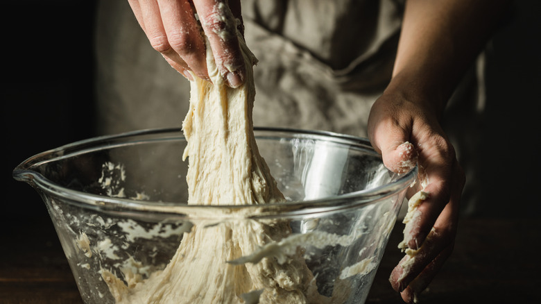 Close-up shot of hands stretching bread dough in a glass bowl