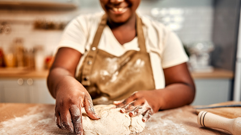 Close-up of a woman's hands as she kneads dough in a kitchen while smiling
