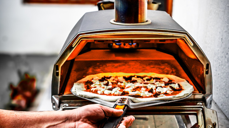 A pizza being launched into a pizza oven on a pizza peel
