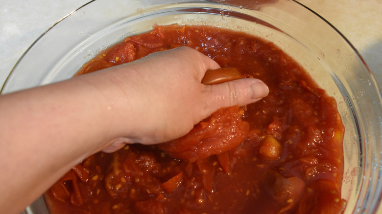 A hand crushing tomatoes in a glass bowl