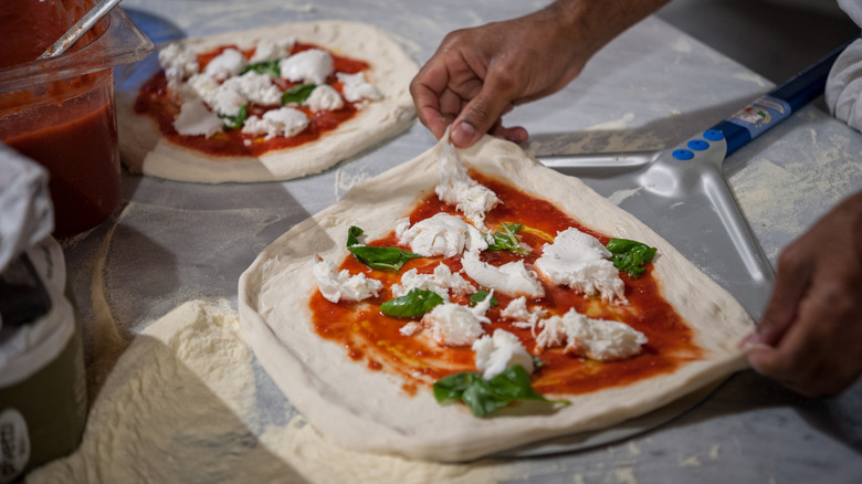A person's hands adding toppings to Neapolitan pizza dough