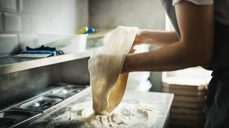 A person stretching pizza dough in a kitchen