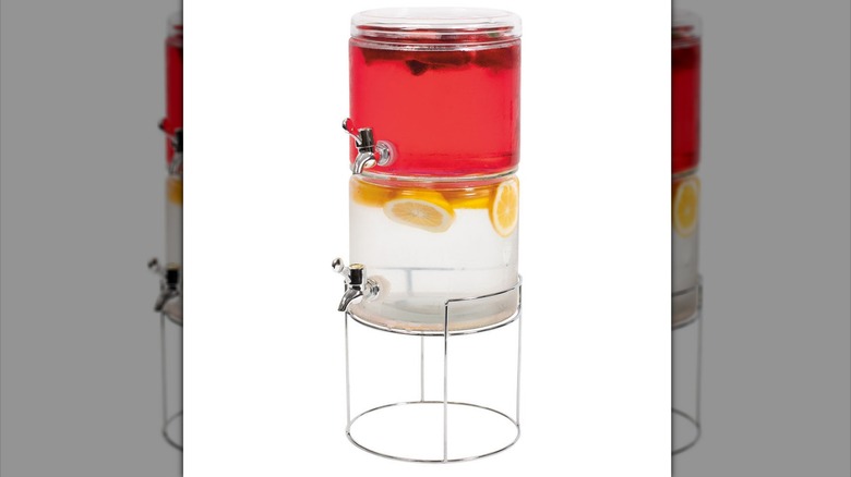 A two-tiered glass beverage dispenser with two spigots containing fruit and liquid.