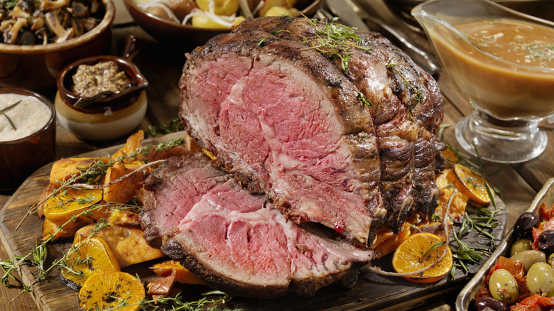 A carving station for a bone-in prime rib roast with several garnishes next to gravy boat