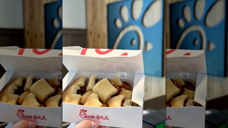 A Chick-fil-A box contains Chick-n-Minis held in front of Chick-fil-A logo inside restaurant.