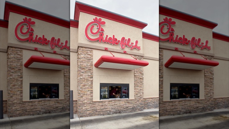 A worker stands in the open window of a Chick-fil-A drive-thru on overcast day.