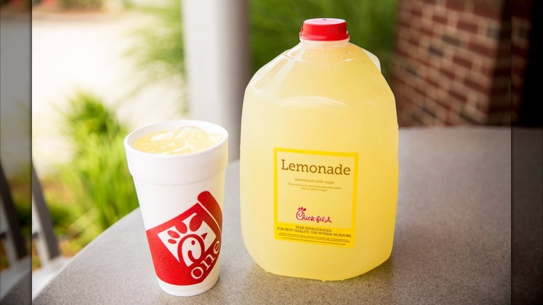 A takeout cup of Chick-fil-A lemonade with ice next to a jug of Chick-fil-A lemonade on outdoor patio table