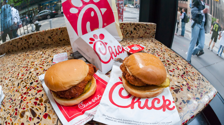 Spicy and Original Chick-fil-A Chicken Sandwiches sit side by side on takeout bags on high top table in restaurant.