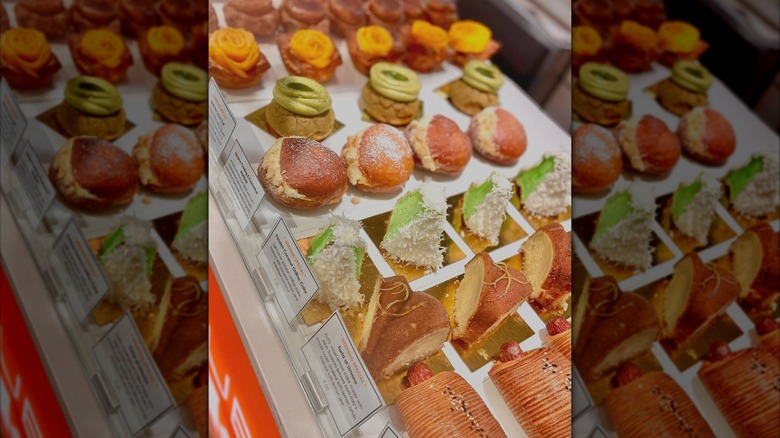 A bakery display case filled with colorful, assorted pastries, including cream puffs, buns, and cake pieces