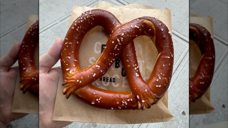 A soft pretzel topped with coarse salt, held in a hand over a paper bag