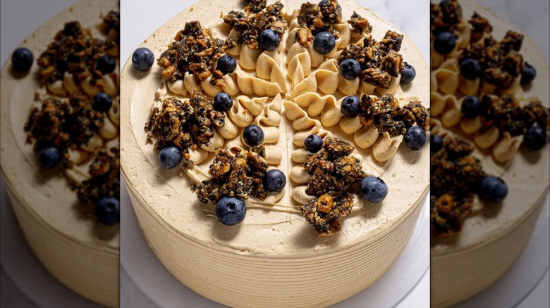 A frosted round cake topped with piped swirls of cream, blueberries, and sesame clusters