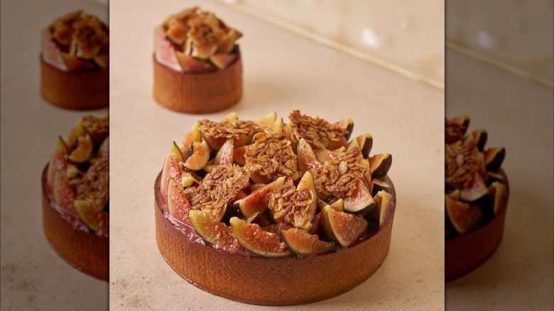 A fig tart topped with sliced fresh figs and granola tuile in a pastry crust with a mini sized one next to it