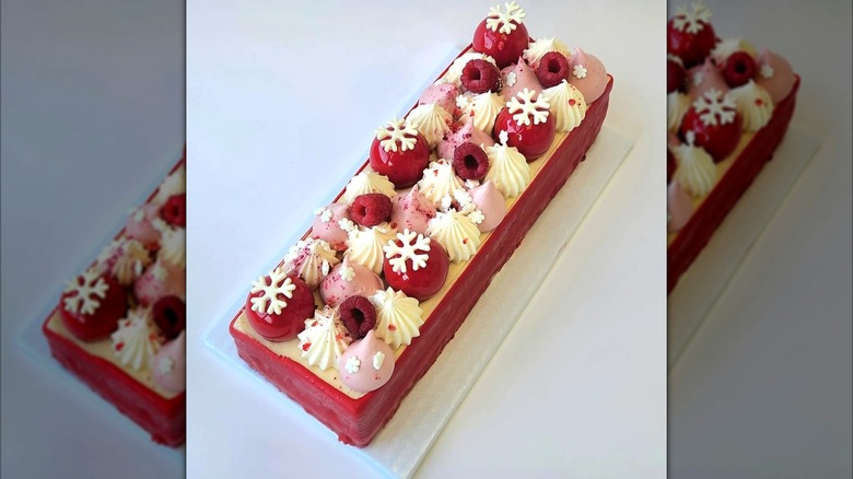 A red-glazed rectangular cake decorated with raspberries, piped cream, and white chocolate snowflakes
