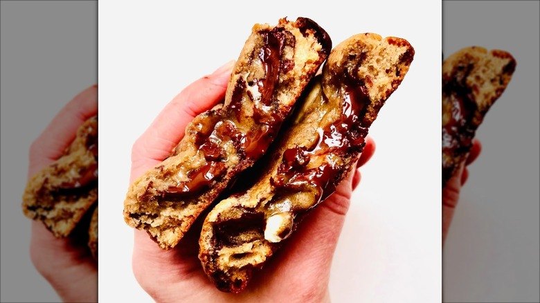 A cookie broken in half with melted chocolate inside, held in someone's hand