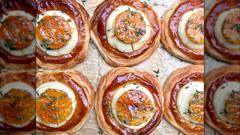Rows of golden, flaky pastries topped with custard, citrus slices, and herbs