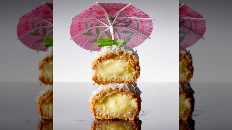 A custard-filled fried pastry cut in half, topped with coconut and a small paper umbrella