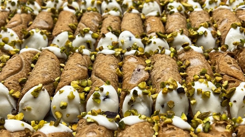 Rows of cannoli shells filled with white ricotta cream and topped with chopped pistachios