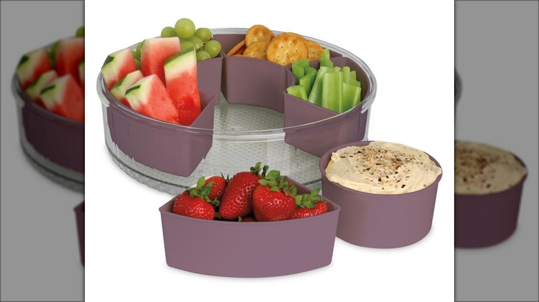Portable snack tray with individual dividers containing crackers, vegetables, hummus, and other snacks.