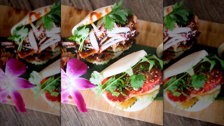 two bao buns stuffed with seasoned meats and topped with sauces and veggies