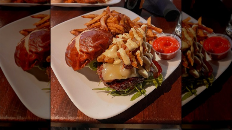 burger topped with cheese, fried food, and drizzle of sauce on plate with fries and ketchup