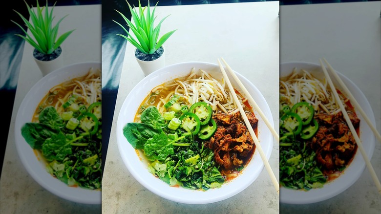 A mexican-style pho bowl with jalapeños, seasoned meat, and veggies, with some chopsticks