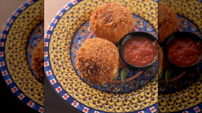 two small arancini rice balls with marinara sauce on decorative plate